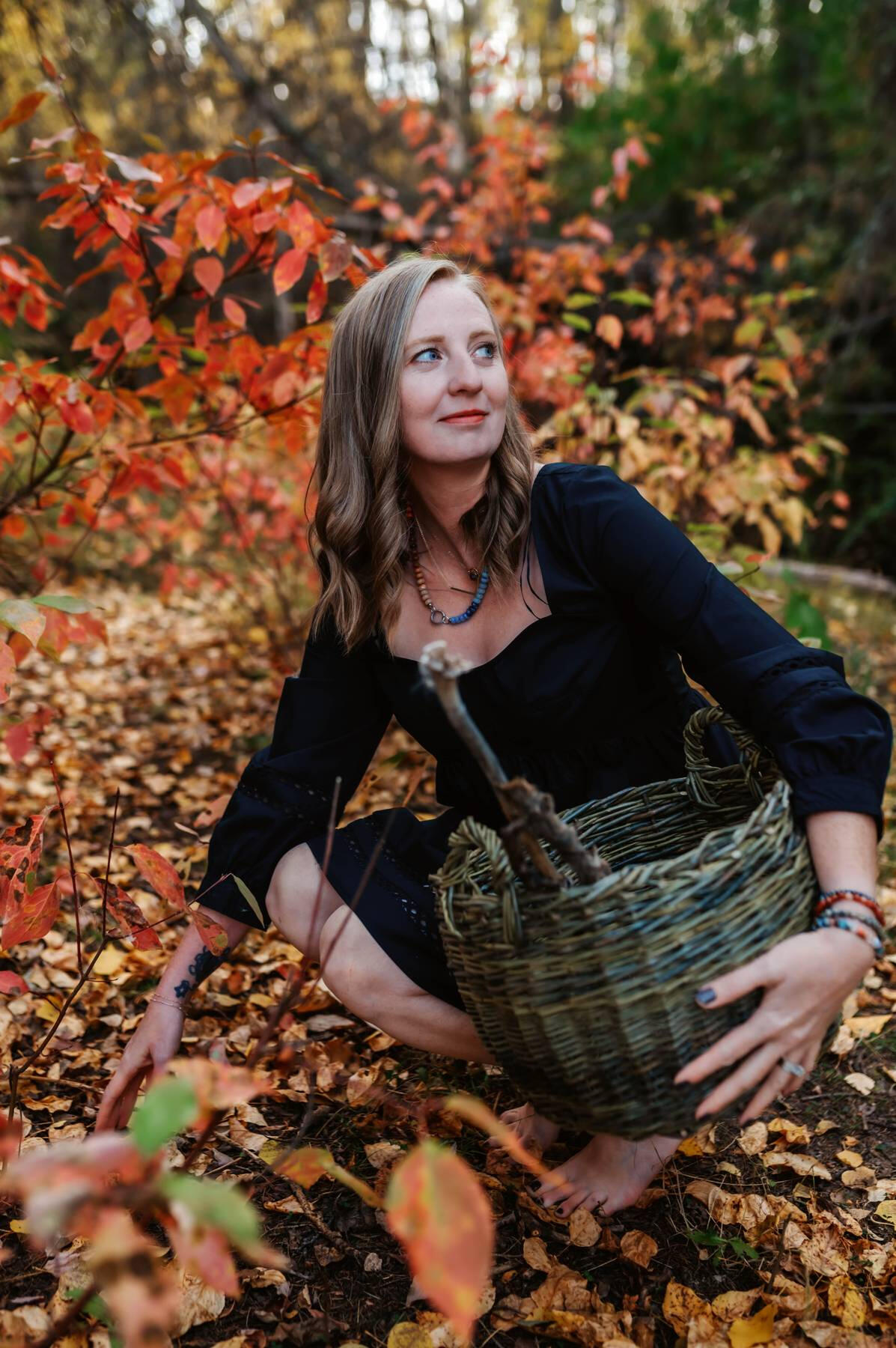 Fall Gathering Basket A woman in a black dress holding a basket gathering leaves, in a fall forest.