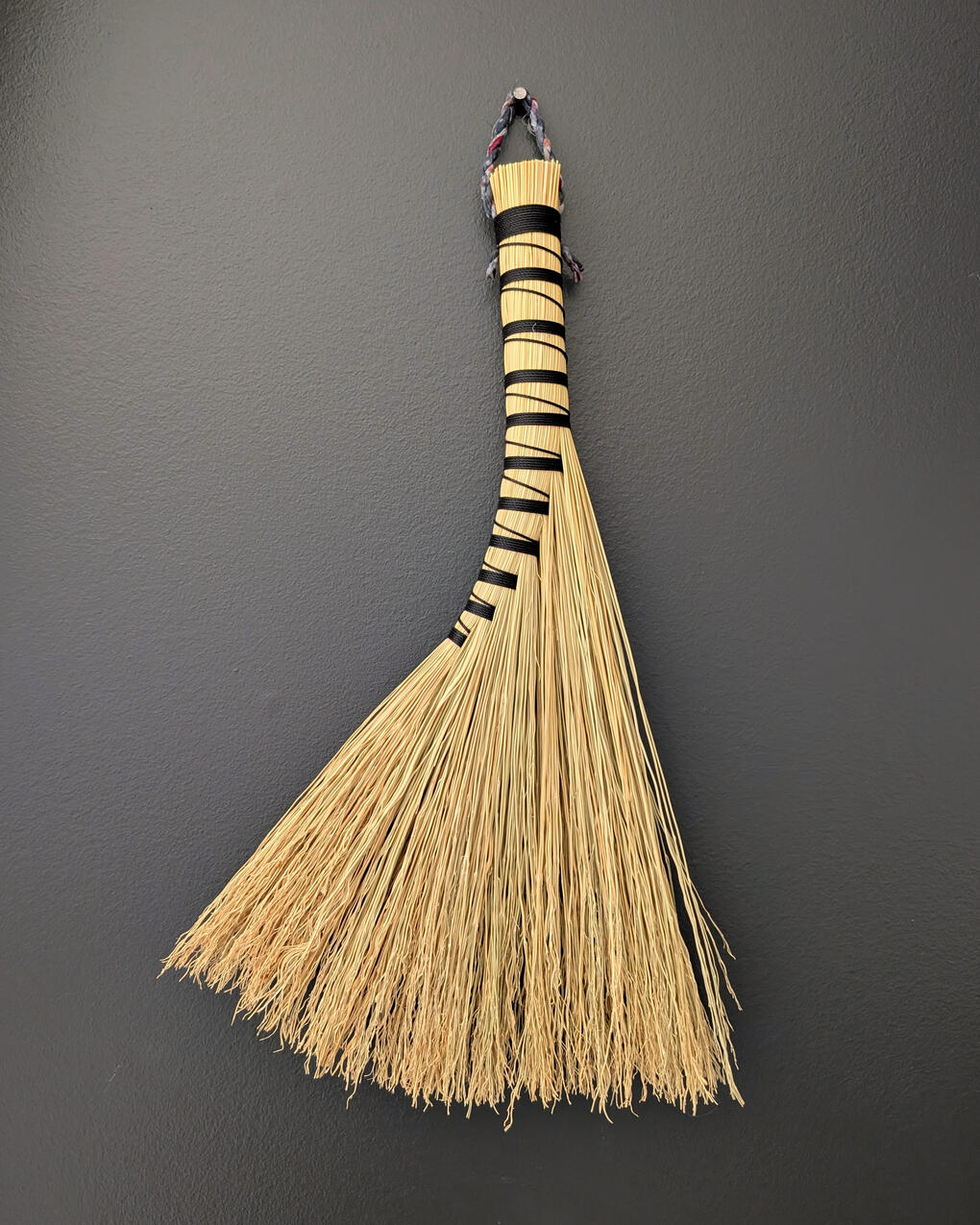 Turkey Wing Handbroom A handbroom bound in black twine, hanging on the wall.