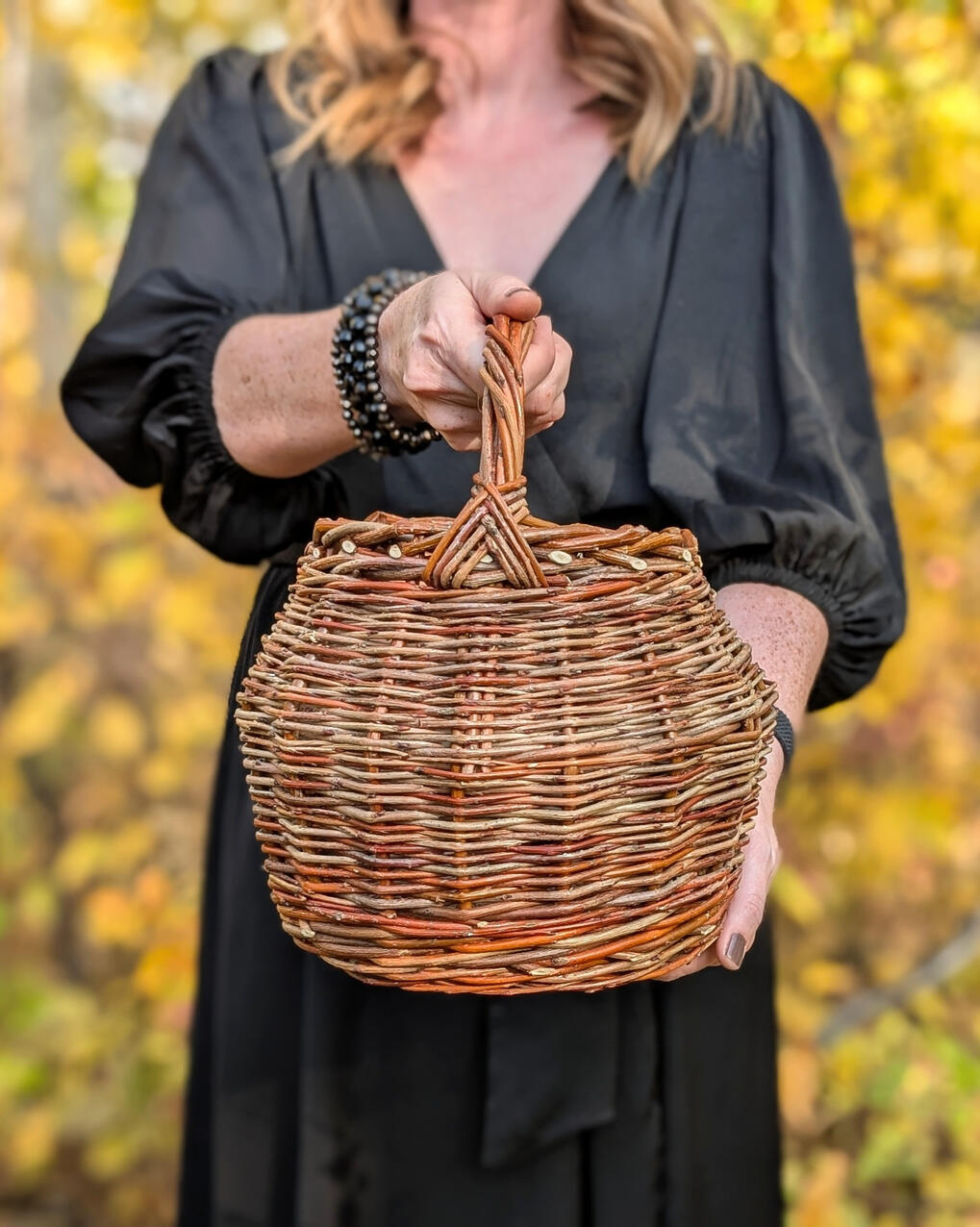 Witch's Cauldron Women in black dress holding willow cauldron shaped basket with background of yellow leaves.