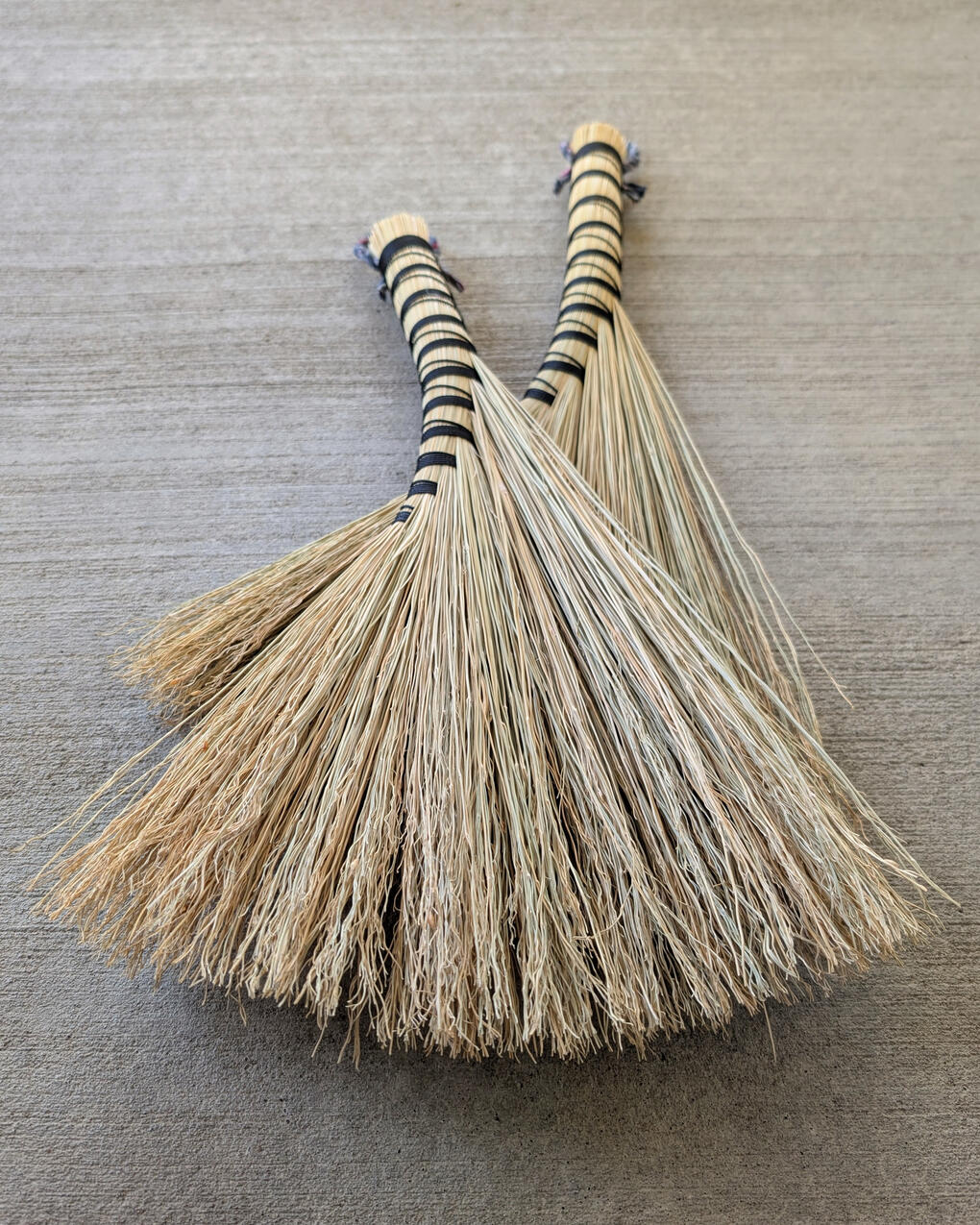 Turkey Wing Handbroom Two handbrooms laying on a concrete background.