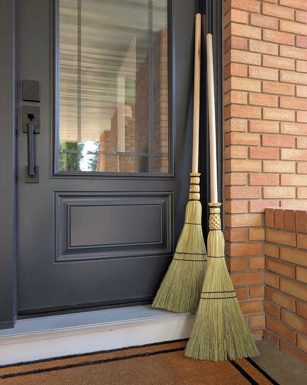 Sweeper Broom Two sweeper brooms leaning against a black door and orange brick.